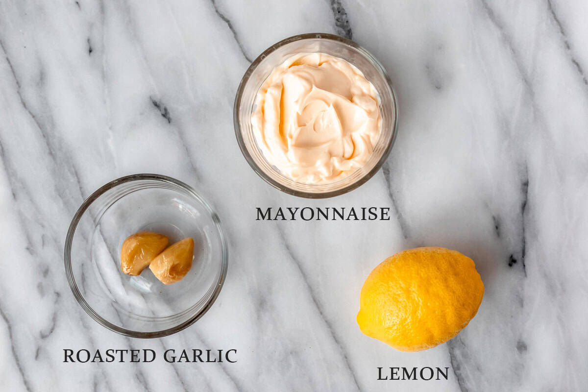 Ingredients needed to make roasted garlic aioli on a marble background with text overlay.