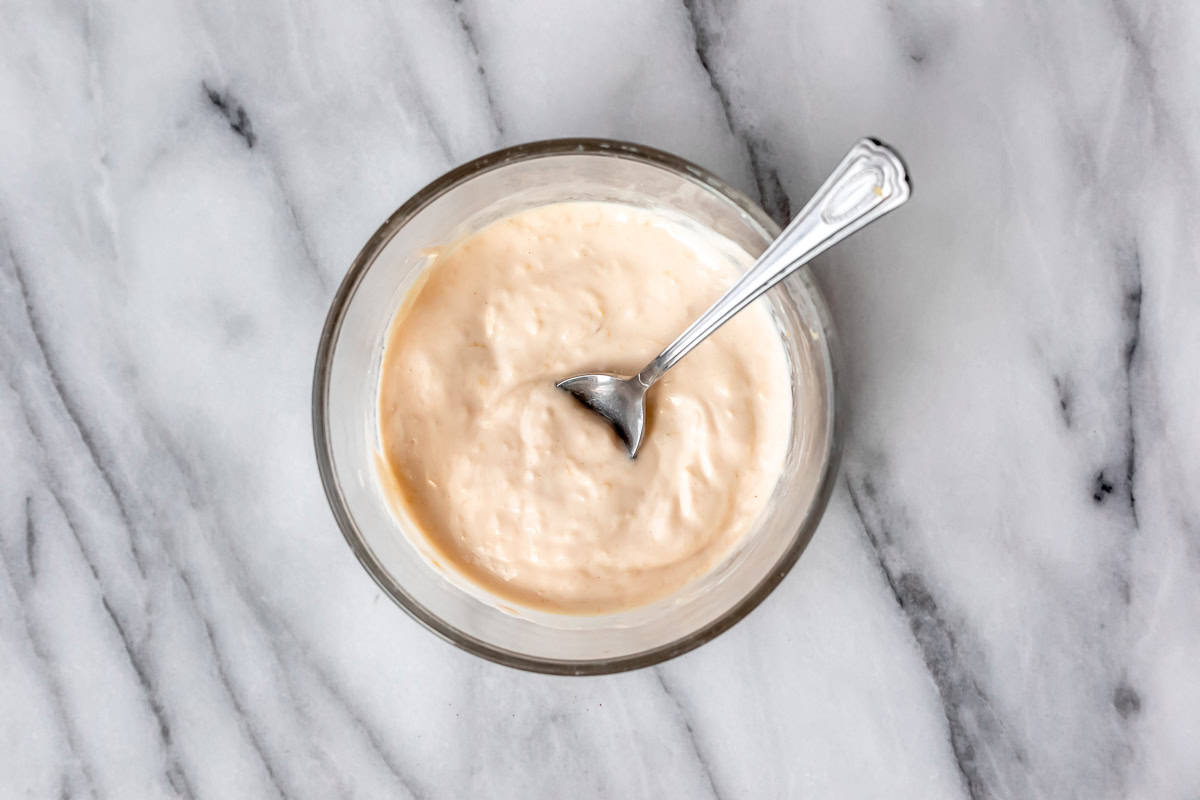 Roasted garlic aioli in a glass bowl with a spoon in it on a marble background.