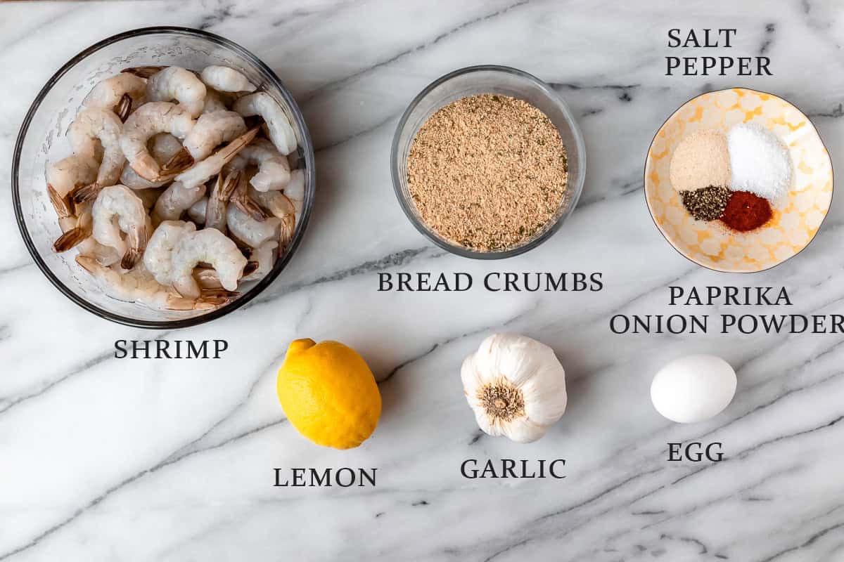 Ingredients needed to make shrimp cakes on a marble background with text overlay.