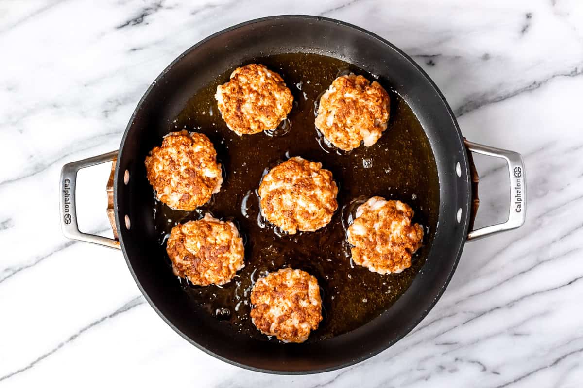 Shrimp cakes frying in a black skillet on a marble background.