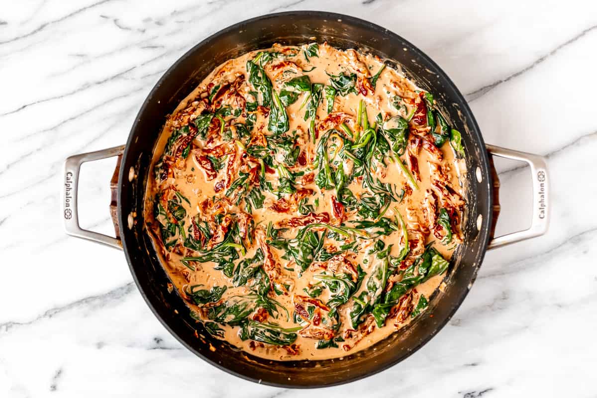 Tuscan cream sauce with sun-dried tomatoes and spinach in a black skillet.