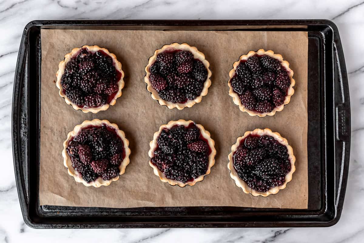 6 baked blackberry tartlets on a parchment paper lined baking sheet.