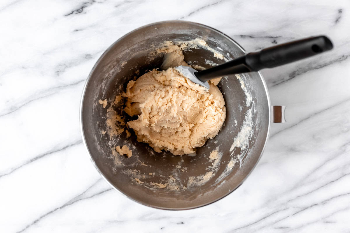 Sweet tart dough, also known as pate sucree, in a silver mixing bowl with a spatula in it.