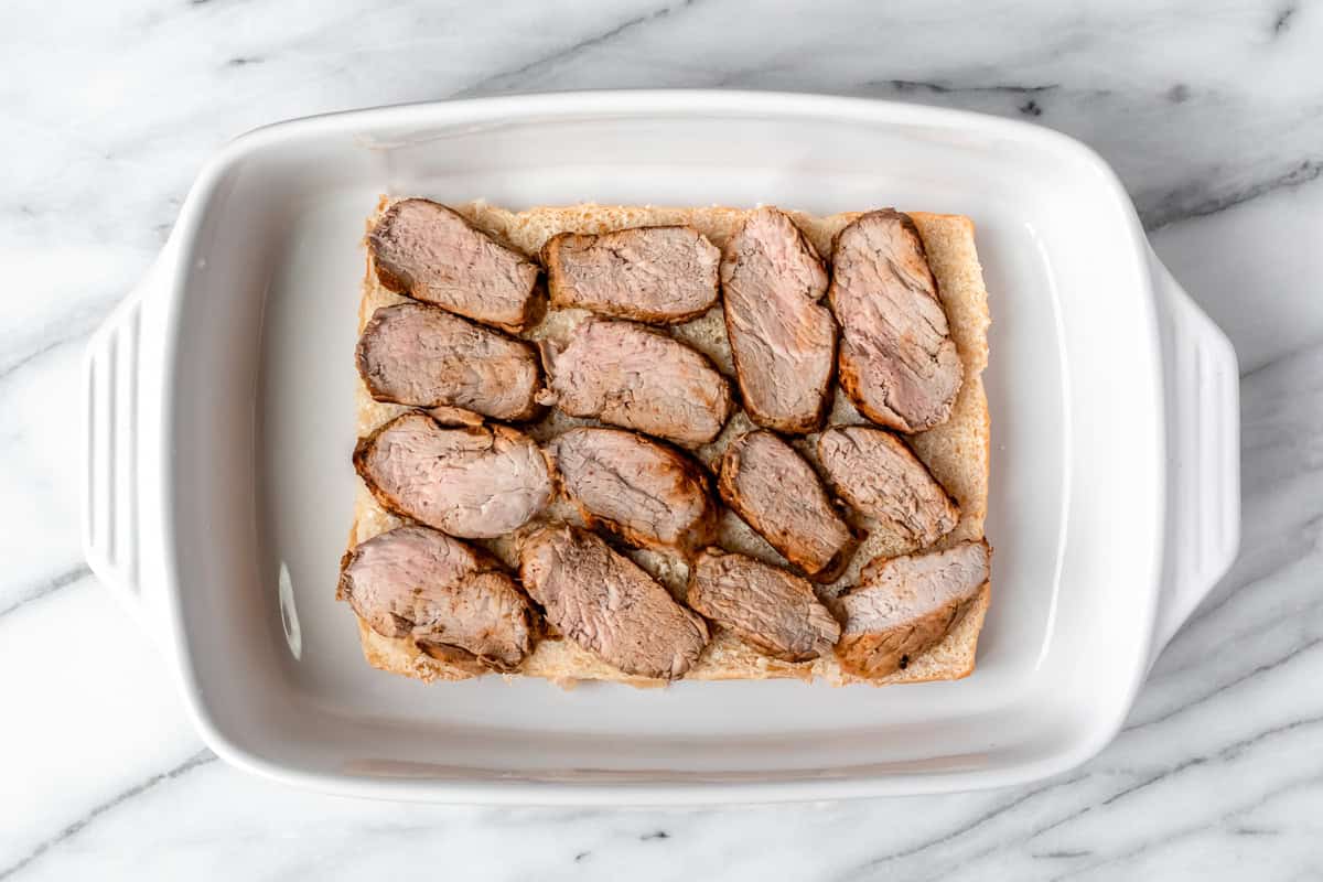 Slider rolls topped with roasted pork in a white casserole dish.