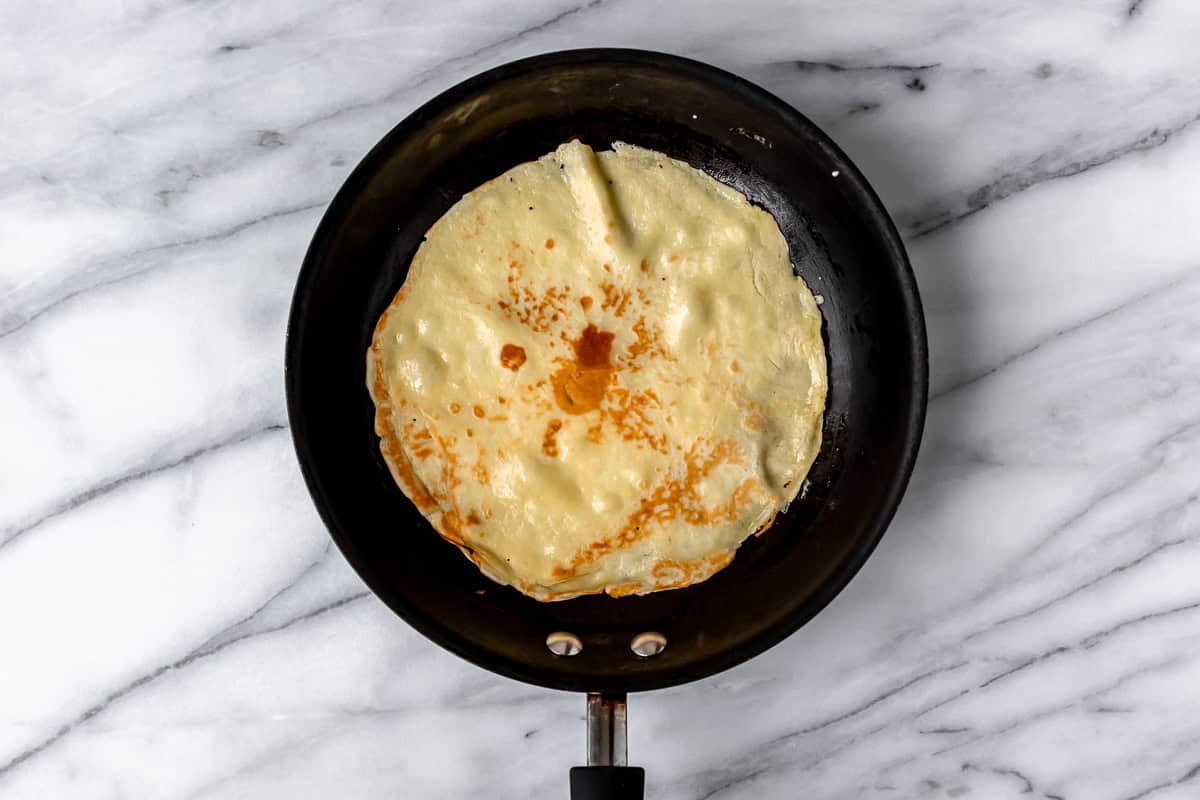 A cooked crepe in a black skillet over a marble background.