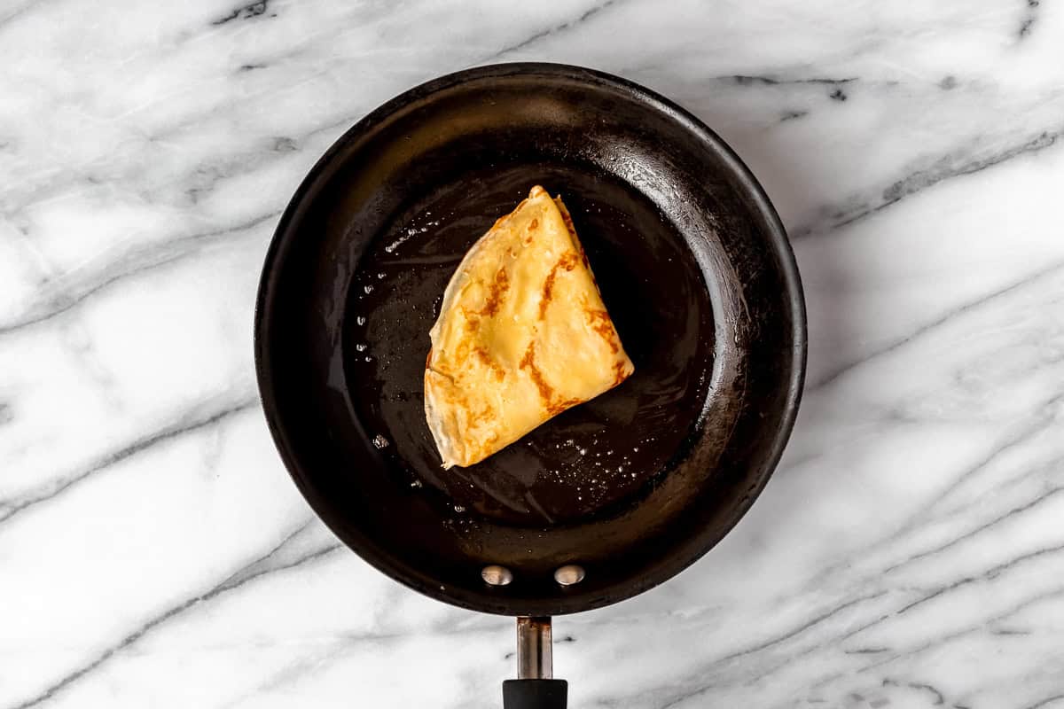 A folded crepe in a black skillet over a marble background.