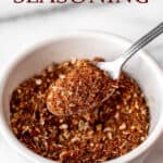 A spoonful of homemade jerk seasoning being held up over a bowl full of more seasoning with text overlay.