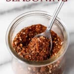 Homemade jerk seasoning in a glass jar with a small spoon in it with text overlay.