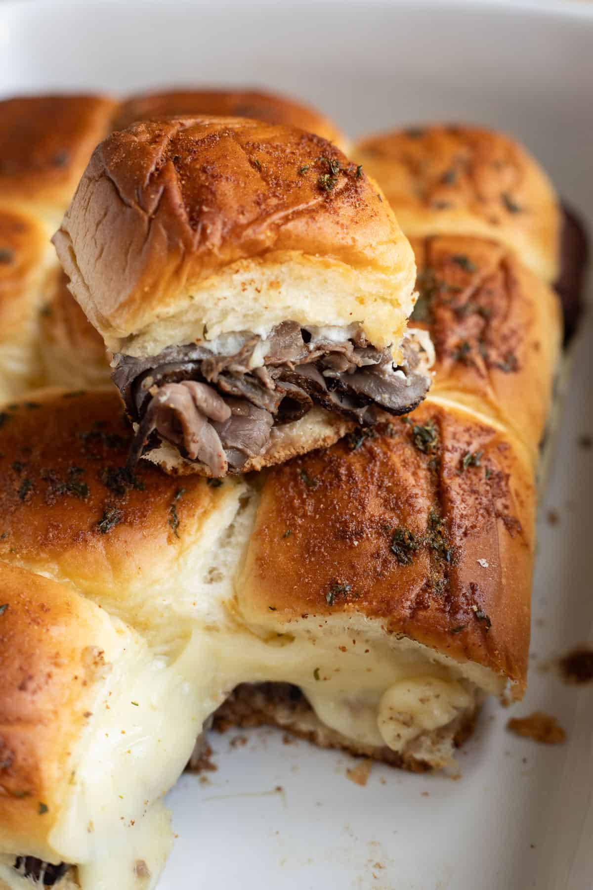 A roast beef slider sitting on top of the remaining sliders in a casserole dish.