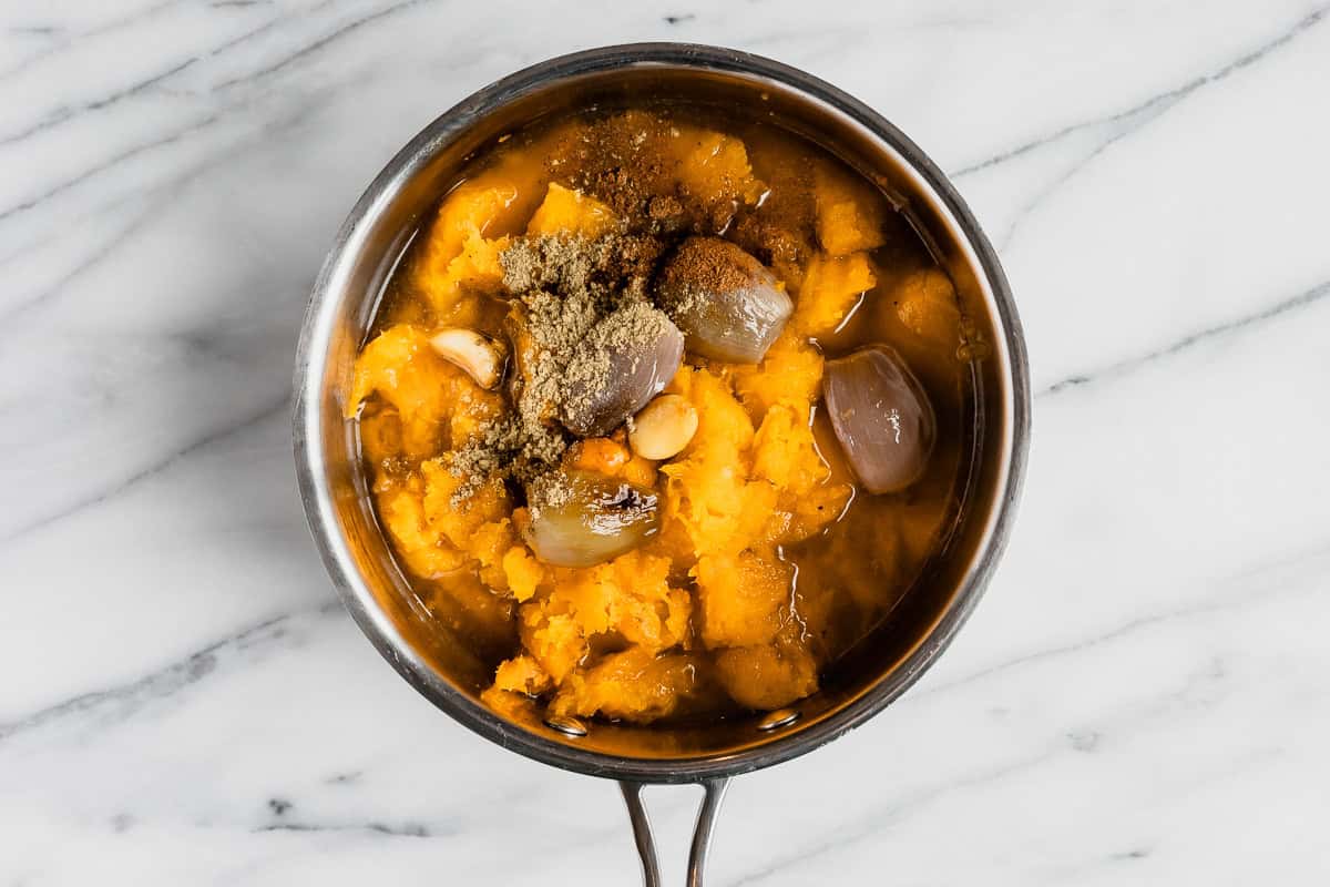 Butternut squash, shallots and seasonings in a silver pot over a marble background.