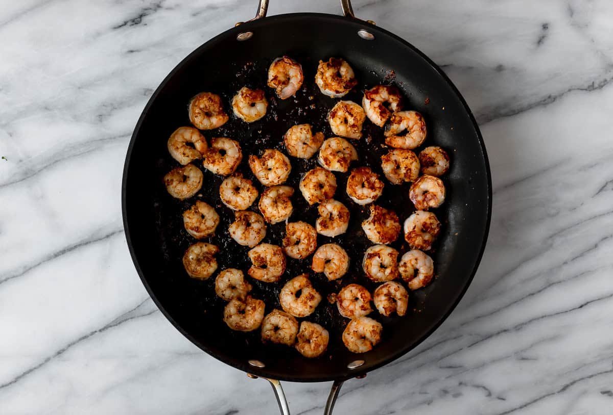 Cooked, seasoned shrimp in a black skillet over a marble background.