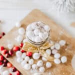Overhead of a jar of candied cranberries on a wood board with more around it with text overlay.