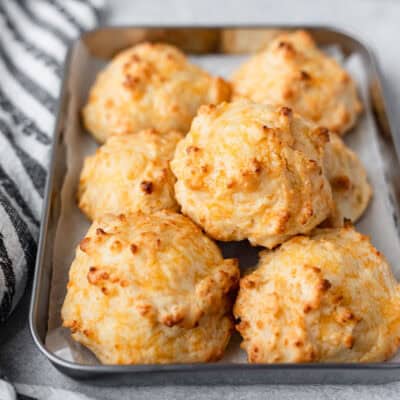 A silver tray filled with cheddar garlic biscuits with a striped towel next to it.