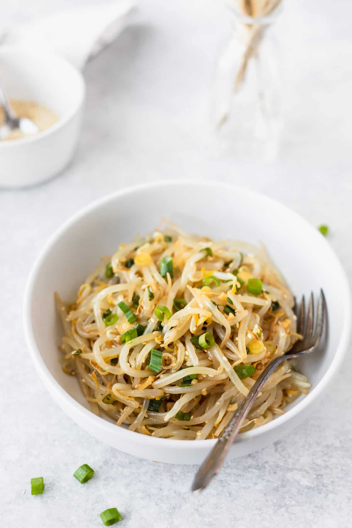 A white bowl filled with Korean bean sprout salad with a fork in it.
