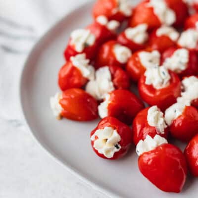 A plate full of cream cheese stuffed peppadew peppers on a white plate over a light background with a striped towel in the background.