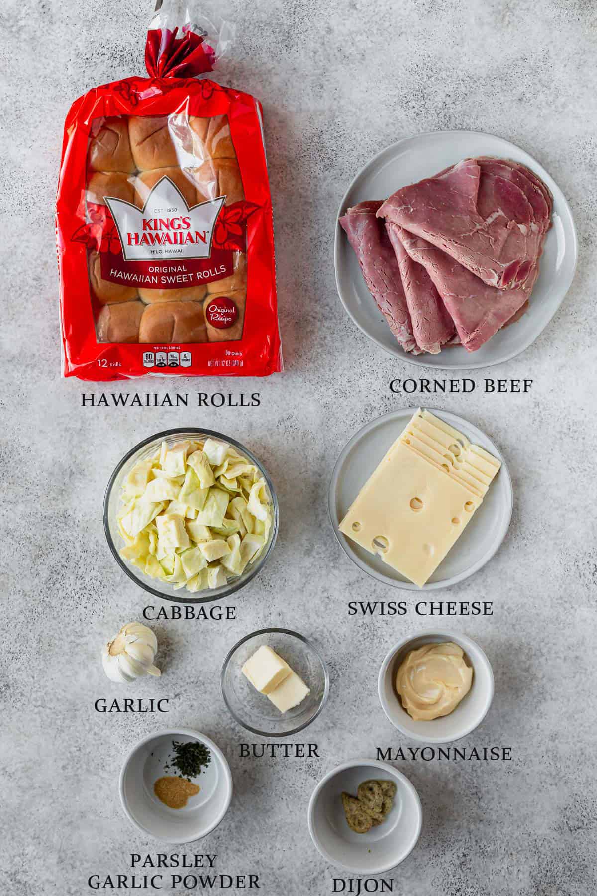 Ingredients needed to make corned beef sliders on Hawaiian rolls on a gray background with text overlay.