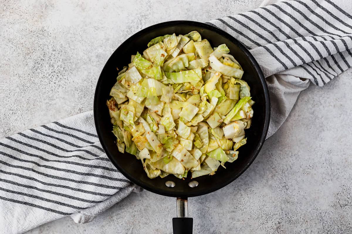 Cooked chopped cabbage in a black skillet over a striped towel.