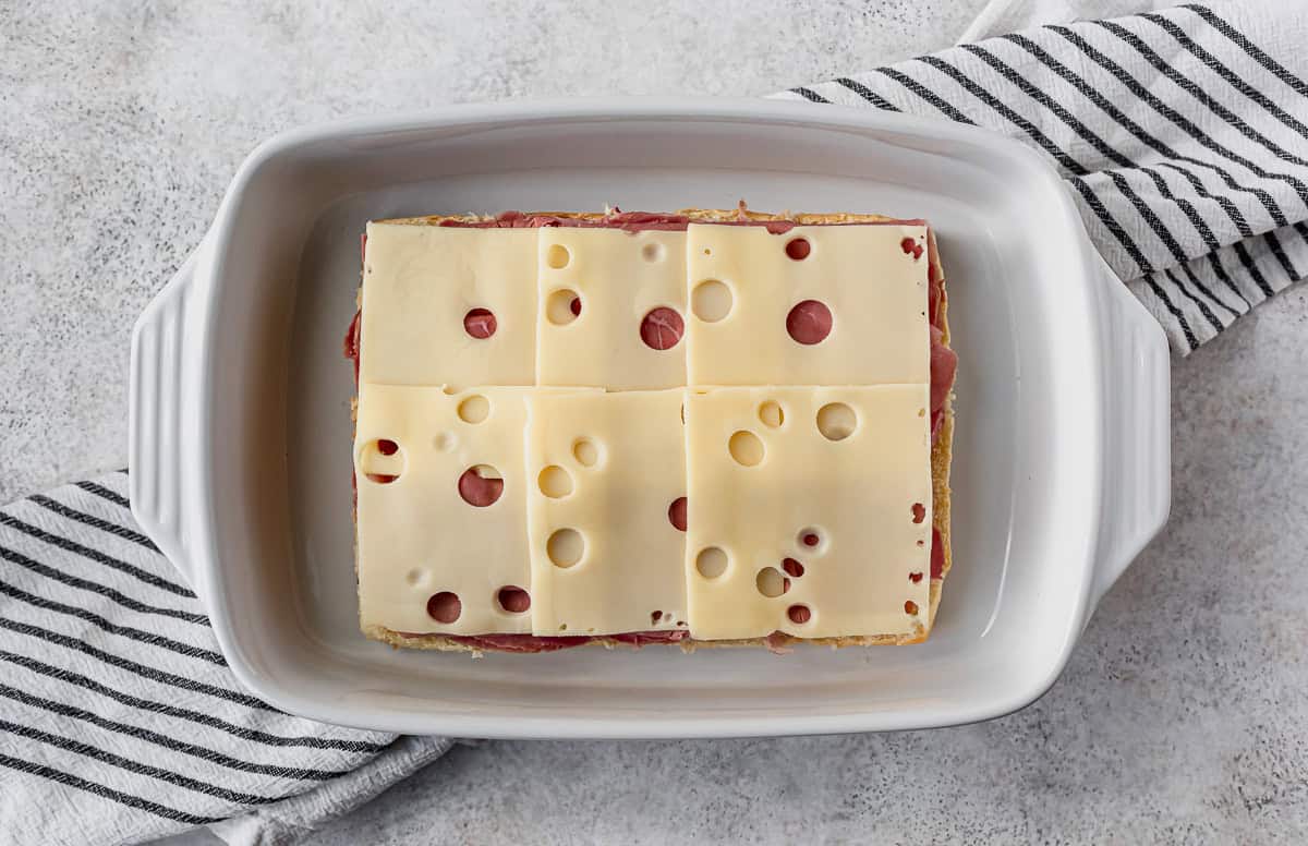 Layers of swiss cheese on top of beef on rolls in a white casserole dish.