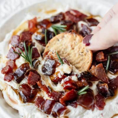 Close up of a cracker being dipped into whipped goat cheese with maple bacon and dates.