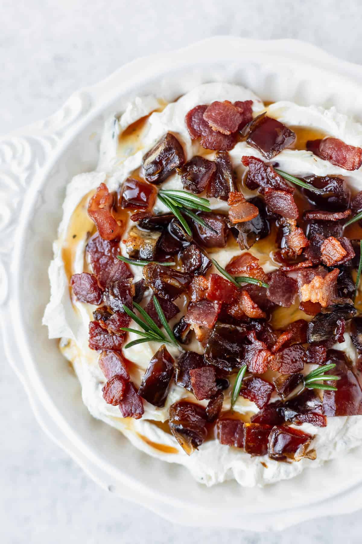 Close up of whipped goat cheese with maple bacon and dates in a white bowl.