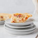 A slice of Italian Easter Pie on a stack of small plates with the rest of the pie and a vase partially showing in the background.
