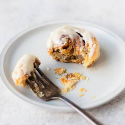 A cinnamon roll on a plate with a forkful next to it on a white plate.