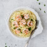 Shrimp Parmesan pasta in a white bowl with a fork in it over a light gray background.