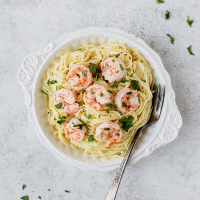 Shrimp Parmesan pasta in a white bowl with a fork in it over a light gray background.