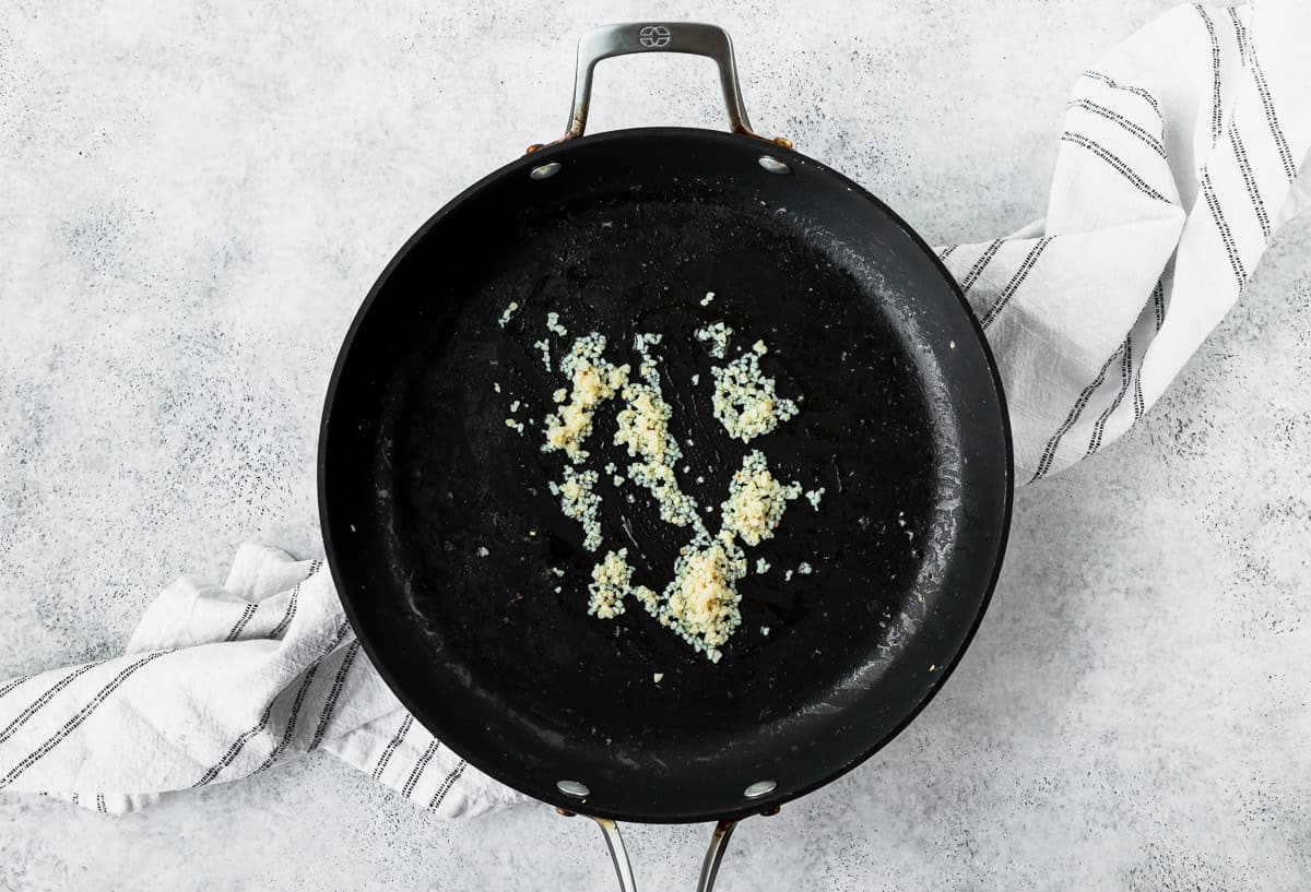 Garlic cooking in a black skillet over a light background.