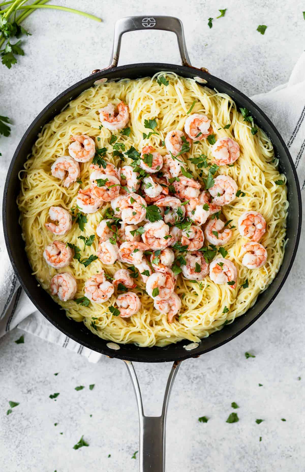 A skillet of shrimp Parmesan pasta in black skillet with parsley all around it.