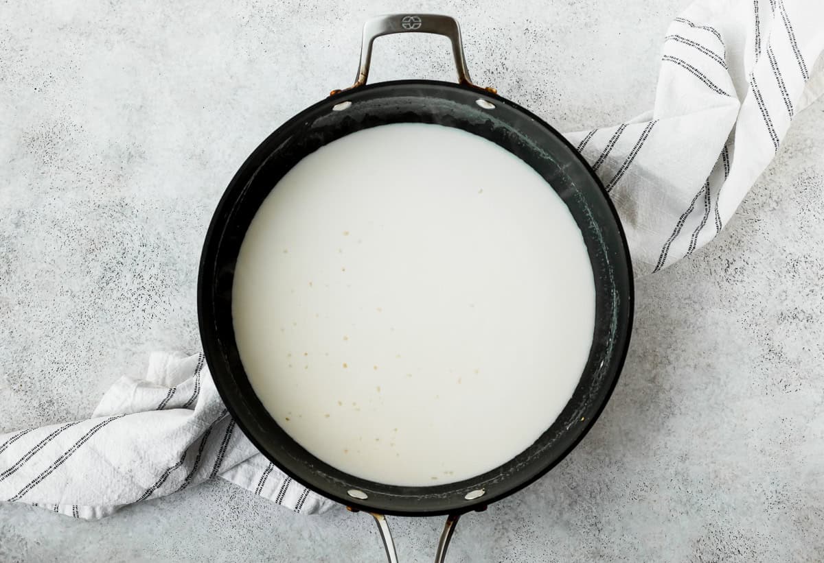 A cream-based sauce in a deep, black skillet over a light background.