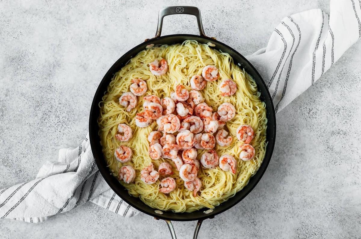 Shrimp and angel hair pasta in a deep, black skillet over a light background.