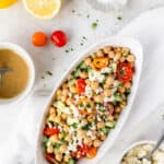 Overhead view of an oval bowl of Mediterranean chickpea salad with ingredients around it with text overlay.