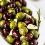 Close up of a bowl of marinated green and purple olives with text overlay.
