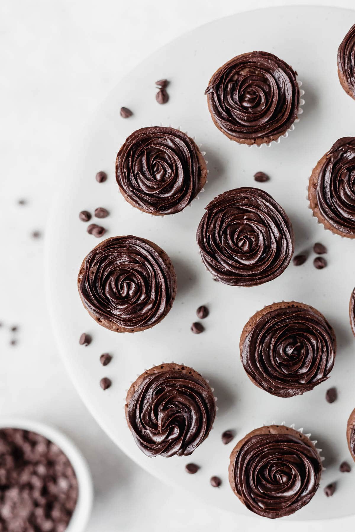 Overhead view of frosted mini brownie cupcakes on a stand with a bowl of mini chocolate chips and loose chips below it.
