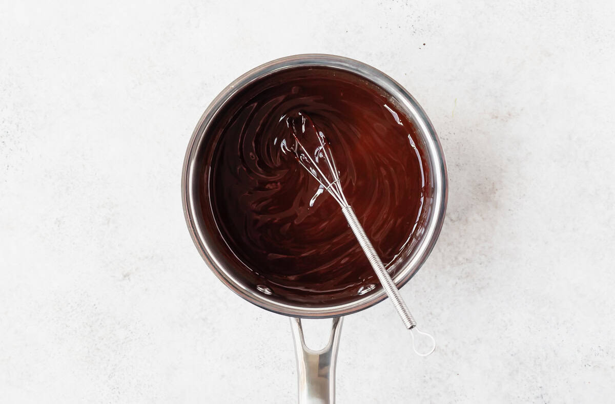 Melted chocolate in a small silver pot with a whisk in it.