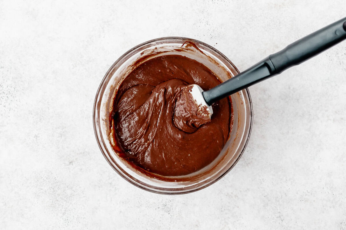 Brownie batter in a glass bowl with a spatula in it.