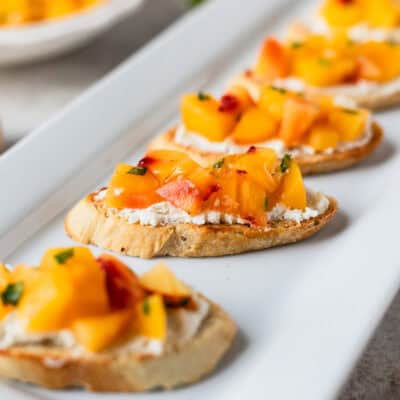 Close up of peach and goat cheese bruschetta on a white plate.