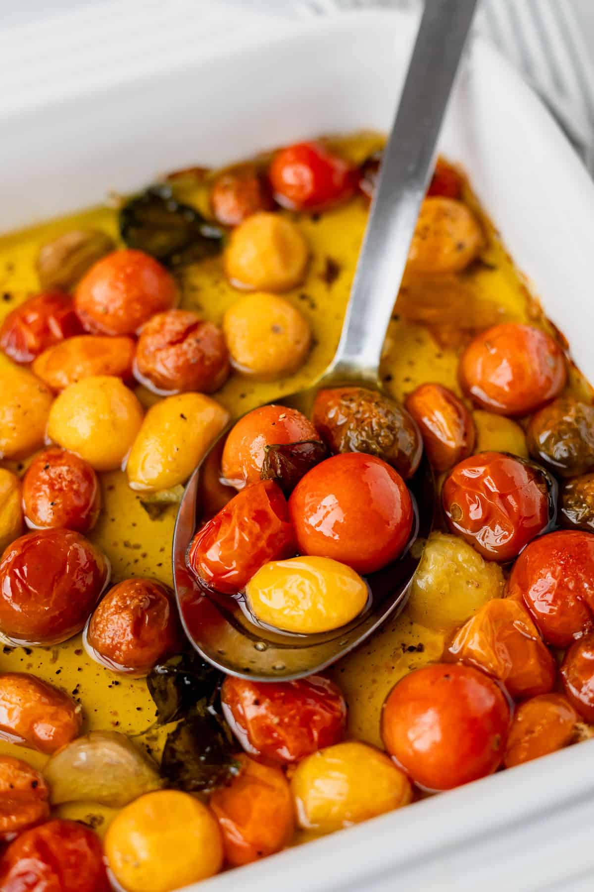 Close up of tomato confit in a baking dish with a silver serving spoon in it.