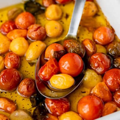 Close up of tomato confit in a baking dish with a silver serving spoon in it.