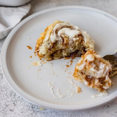 A puff pastry apple cinnamon roll cut in half on a white plate.