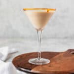 A creme brulee martini on a wood board with a white linen in the background.