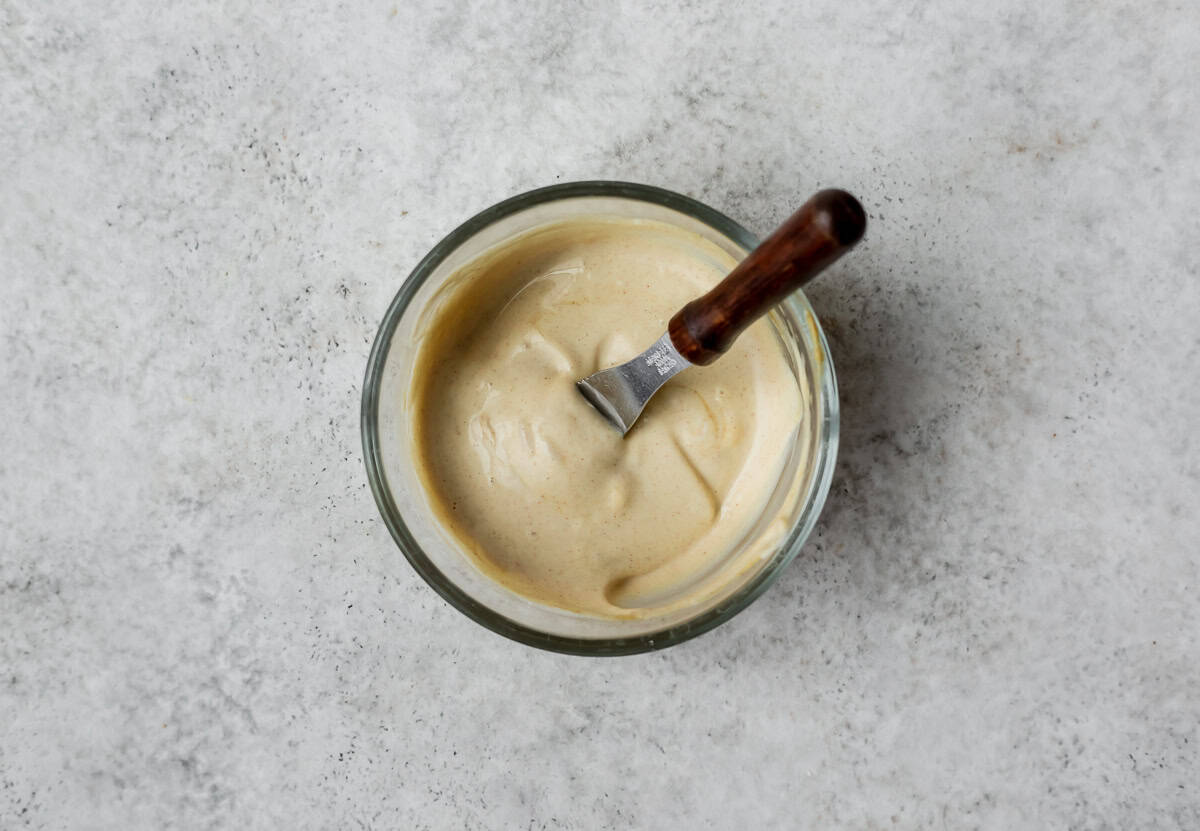 Dijon and mayonnaise spread in a small glass bowl with a spreader in it.