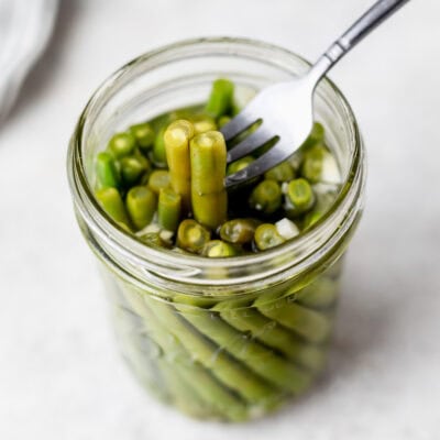 A small fork pulling up pickled green beans from a mason jar.