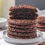 A stack of fudgy brownie cookies with the three on top cut in half to show the inside.