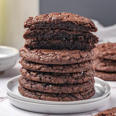 A stack of fudgy brownie cookies with the three on top cut in half to show the inside.