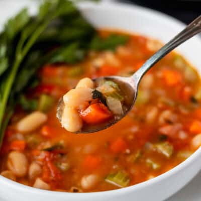 A spoonful of Tuscan white bean stew being held up over a bowl.