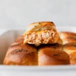 A buffalo chicken slider on top of the rest of the sliders in a white casserole dish.