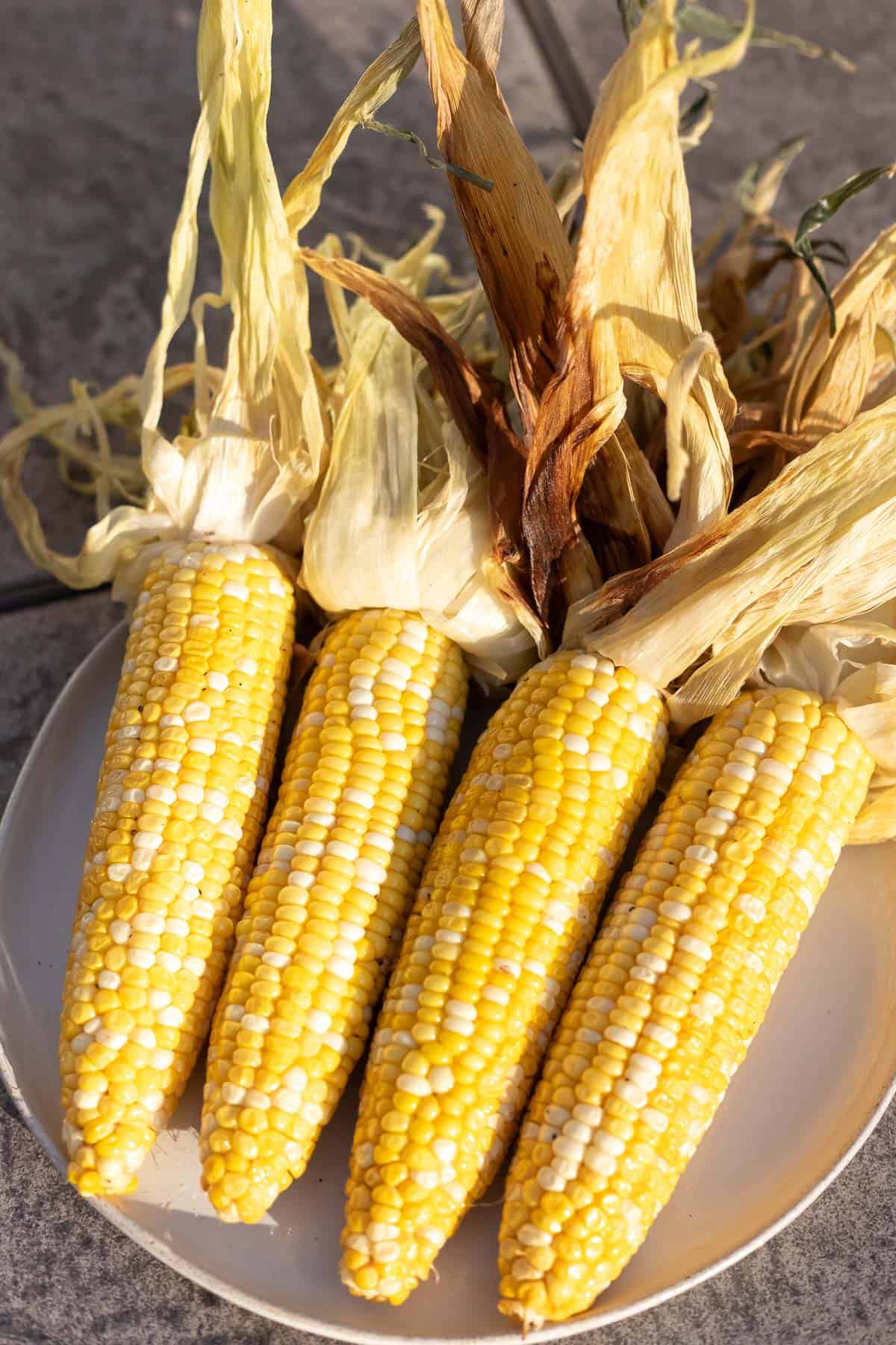 Overhead view of 4 ears of smoked corn on the cob on a tan plate.