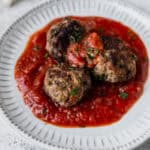 Three Italian meatballs in sauce on a small white plate.